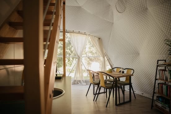 Minimalist interior with wooden chairs and table near large windows, white walls, and natural light streaming in