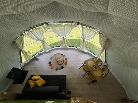 Interior overhead view of a mesh tent with wooden floor containing drums, cushions, and musical instruments arranged inside
