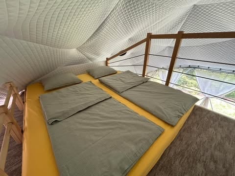 Modern loft bedroom with yellow bed frame, gray bedding, wooden railing, and geometric white ceiling with skylights