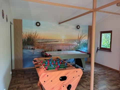 Recreation room with foosball table, ping pong table, and beach sunset mural on wall