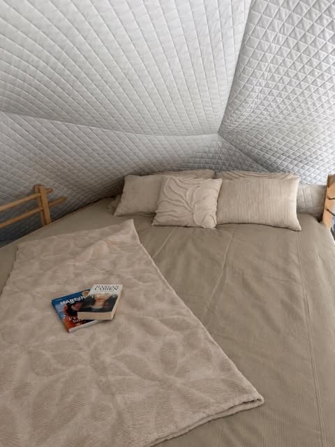 Cozy bedroom nook with quilted white walls, beige bedding, decorative pillows, and a magazine on the bed