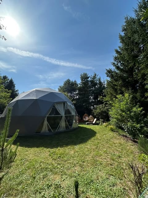 Black geodesic dome tent in a grassy garden surrounded by trees under blue sky