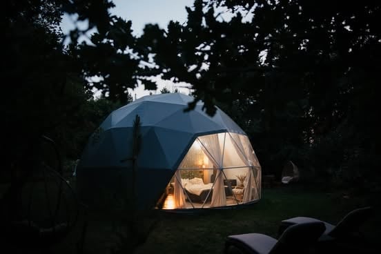 Illuminated geodesic dome tent glowing at night surrounded by dark trees and foliage